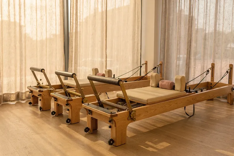 Sala de pilates con máquinas Reformer de madera junto a ventanales con cortinas de lino